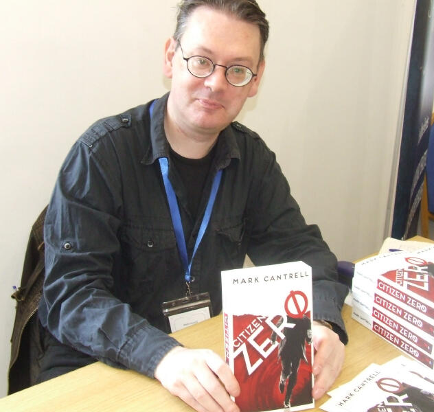 Mark Cantrell dressed in a black shirt holds a copy of his novel Citizen Zero.